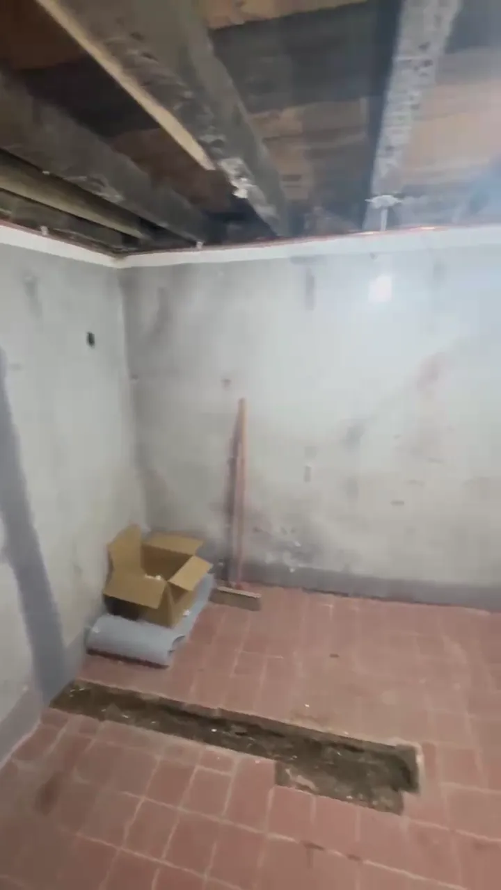 Lower level room before work, with bare walls and exposed joists
